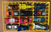 Top view of 12 retro Hot Wheels cars in yellow tray showing various colors and custom details such as flames and visible engines