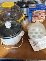 Photo of all items on table including crock pot, fondue set, egg cooker, stuffed burger maker, kitchen scale, and leftover boxes