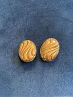 Photo of front sides of two oval-shaped earrings with a raised wavy wave design pattern.