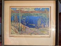 Framed Tom Thomson print showing a vibrant landscape with water, trees, and rocks.