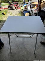 Drafting table with flat viewing surface and tubular metal legs in open garage.