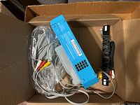 Box with aqua blue Nintendo Wii console, AV cables, and sensor bar inside, viewed from above.