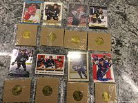 Full view of 11 hockey player cards arranged in three rows with 9 gold-tone commemorative coins in sealed cardboard holders placed between and below the cards, all on granite countertop.