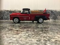 Side view of red and black 1957 Fargo pickup truck model with Canadian Tire logo and wooden crate load, on granite countertop.