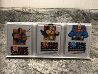 Front view of three unopened DC Cosmic Cards packs featuring Deathstroke, Wonder Woman, and Superman on the packaging.