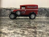 Side view of red Motorcraft Racing Ford Model A Delivery Van coin bank showing number 15 decal on the door, silver wheels, black accents, on granite surface against white background.