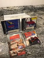 Photo showing two PlayStation1 game cases for ESPN Extreme Games and Tiger Woods 99 PGA Tour Golf along with their instruction booklets laid on a granite countertop.