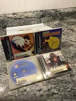 Four PlayStation 1 sports games displayed on a countertop, including NFL Quarterback Club, NBA Jam, NBA Jam Tournament Edition, and All-Star Slammin' D-Ball in jewel cases.