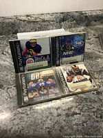 Photo showing 4 PlayStation1 sports games with visible cover art featuring NCAA Football, NHL Hockey, NBA Basketball, and Madden Football in original jewel cases.