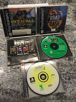 Four PlayStation 1 games in cases or holders showing front covers and discs: Pitball, Road Rash 3D, NFL Quarterback Club, Street Sk8er 2.