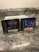 Photo showing two PlayStation 1 game jewel cases: Beyblade and Ball Breakers, placed on a granite countertop.