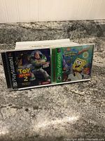 Photo of two PlayStation 1 game cases: Toy Story 2 and SpongeBob SquarePants games on a granite countertop.