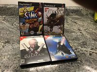 Photo showing four PlayStation 2 game cases: The Sims Bustin' Out, Conflict Vietnam, Hitman, and a Star Wars game.