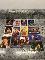 Photo showing 14 wrestling cards laid out on a granite surface. Cards depict various wrestlers in different action poses and portraits. Included wrestlers like Hulk Hogan, Rick Rude, and Jimmy Snuka visible.