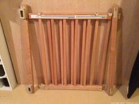 Wood baby gate with vertical slats and four mounting brackets attached on the sides for installation.