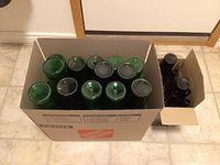 Two cardboard boxes containing about 30 clean green glass wine bottles, viewed from top down showing bottle openings and bases.