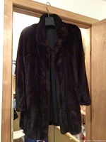 Photo of a dark brown muskrat fur coat hanging on a hanger, showing the front view, collar, and long sleeves.