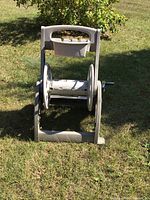 Front view of a plastic hose caddy reel sitting on grass with a handle and crank mechanism, showing the hose reel frame.