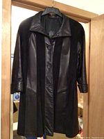 Black leather coat hanging on a hanger on a door, showing front button closure and collar.