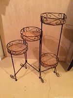 Front view of the 4-tier black metal plant stand with circular wooden shelves and decorative scrollwork on frame and feet.