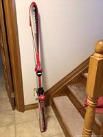 Adult downhill skis standing upright showing details of the Rossignol brand and bindings attached, placed near a staircase inside a home.