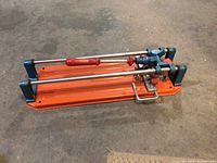 Orange base manual tile cutter with metal rods and red scoring handle