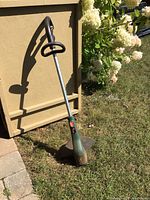 Black and Decker electric corded string trimmer standing upright outside against a beige wall with grass and flowers around.