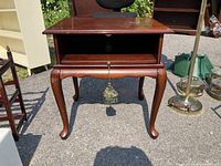 Dark wood Bombay Company television stand outdoors, showing front view with curved legs, open shelf, and drawer with tassel pull.
