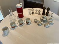 Full lot layout showing coffee mugs, espresso cups with saucers, salt and pepper mills and shakers, water decanter, and thermos on table.