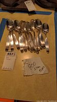 Overview of 11 .800 silver spoons laid out on table with seller tags