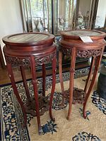 Pair of reddish-brown carved wood accent tables with round stone tops, standing side by side on a carpeted floor near a china cabinet.