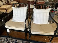 Two black wooden frame armchairs with beige removable seat cushions and light blue removable back cushions placed on a hardwood floor and patterned rug.