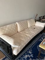 Full side view of Asian style couch showing light beige cushions with circular pattern and black wooden frame.
