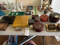 Full table view showing 14 Asian inspired enamel and lacquered boxes in rectangular, round, and square shapes with different designs and colors.