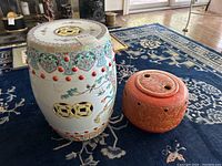 Full view of porcelain garden stool and round ceramic planter with lid placed next to each other on blue patterned rug
