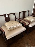 Two matching carved wood armchairs side by side with seat cushions and decorative pillows