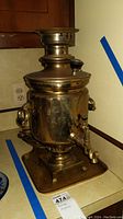 Front perspective showing the polished metal samovar with attached tray, spout, and decorative handles.