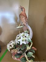 Full view of Boehm porcelain bird statue with detailed white lilies and surrounding leaves on a branch base.
