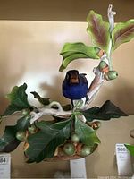 Overall front view of blue bird perched on oak branch with green leaves and acorns.