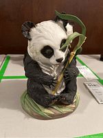 Front view of Boehm porcelain panda statue sitting and holding bamboo stalk.