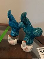 Set containing two large blue rooster figurines and two smaller white chicken figurines with red Asian characters printed on them, placed on a reflective surface for visual documentation.