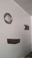 Three Mercedes accessories mounted on wall: circular hubcap on top left, two different Mercedes front grilles below and to the right.