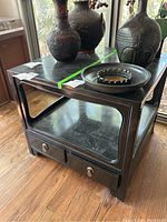 Front view of dark wood side table with two drawers and decorative items on top showing scratches on surface.
