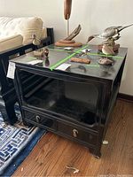Full view of the black wooden side table with various decorative objects on top, glass inset surface visible with wear and scratches.