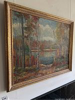 Side angle view of the framed landscape oil painting showing wooded area and water body.