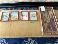 Five framed oil paintings on canvas laid out on a bench; four small landscape scenes and a larger Venetian street canal scene.