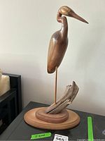 Front view of the signed wooden crane sculpture showing the detailed carving and wooden base with driftwood.