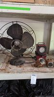 Rusty Westinghouse vintage electric fan, fuel pump pressure gauge, and two Craftsman water meters on a dusty shelf