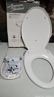 Full view of the American Standard AquaWash bidet seat with packaging and installation components in plastic bag.