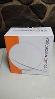 Front view of the boxed Circadian Optics bright light therapy lamp showing white and orange branding with product image.